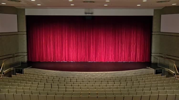 Oswego High School Auditorium stage with red curtain closed, light on the orchestra pit, and empty front section of seating. 